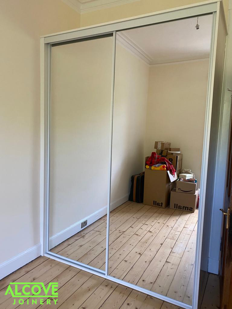 Bespoke fitted sliding wardrobe. Sliding Two door-set - white traditional frame with full panel silver mirror. Interior constructed using white melamine faced furniture panel incorporating hanging and shelving.