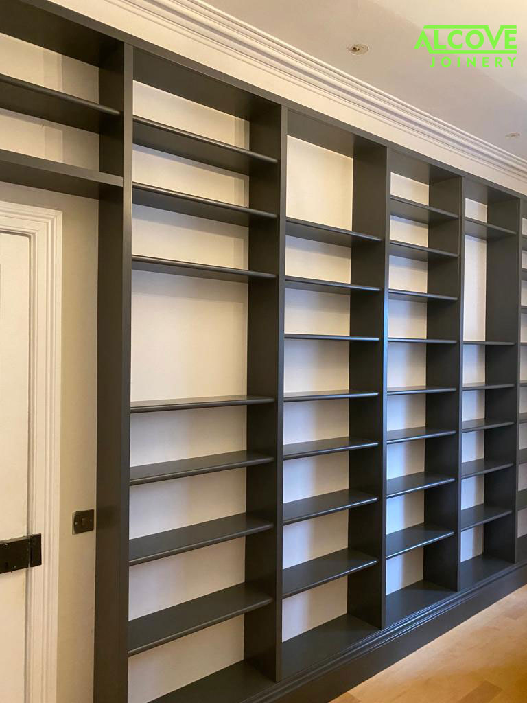Fully spray finished bespoke bookcase installed along a 4m wall and continuing above the doorway. Spray finish - dark navy blue - Vulcan.